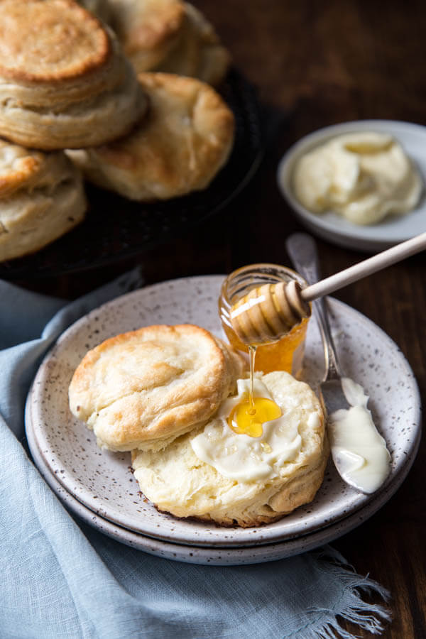 A split open biscuit on a plate with butter and honey