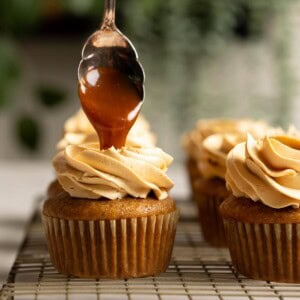 Spooning caramel on top of a frosted caramel apple cupcake.