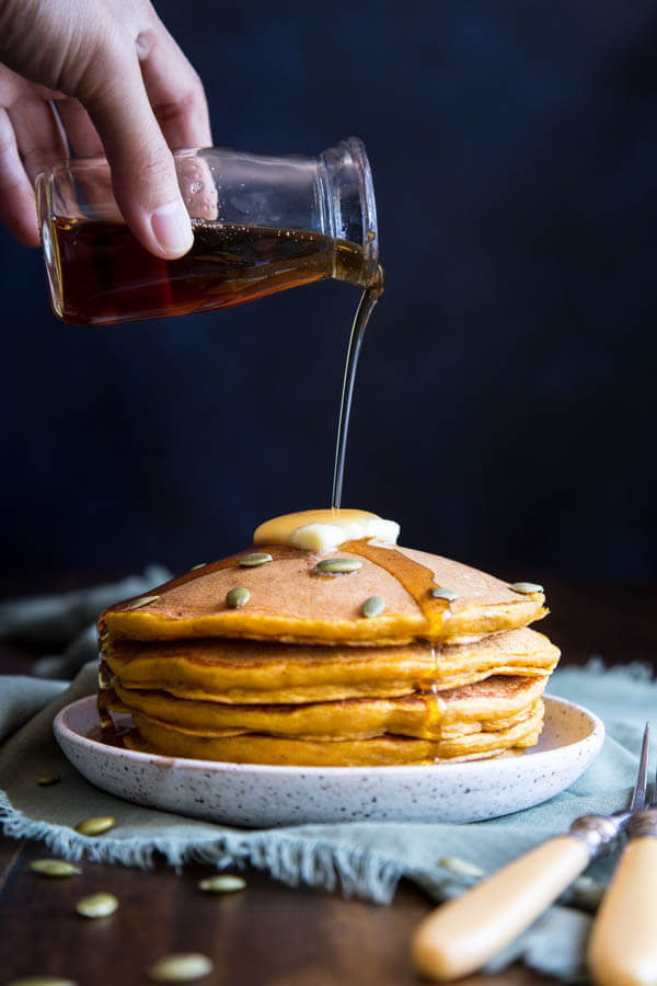 Pouring maple syrup on a stack of pumpkin pancakes