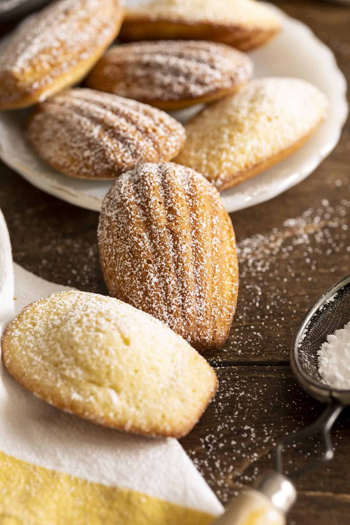 Madeleine cookies on a plate with two on the table top.