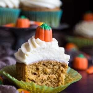 A half eaten pumpkin pie cupcake with cream cheese frosting.