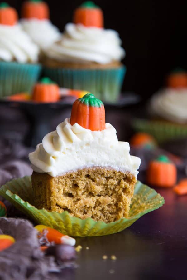 A half eaten pumpkin pie cupcake with cream cheese frosting.