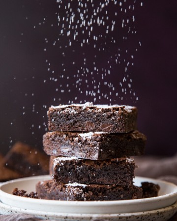 A stack of homemade brownies being dusted with powder sugar