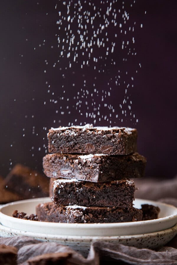 A stack of homemade brownies being dusted with powder sugar