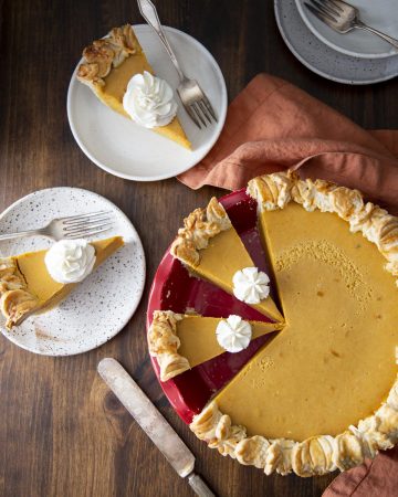 A pumpkin pie in a red pie dish and slices of pumpkin pies on plates