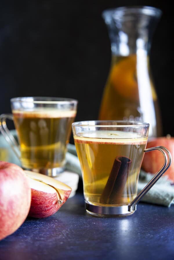 2 glasses of apple ciders next to some apple and a serving jug.