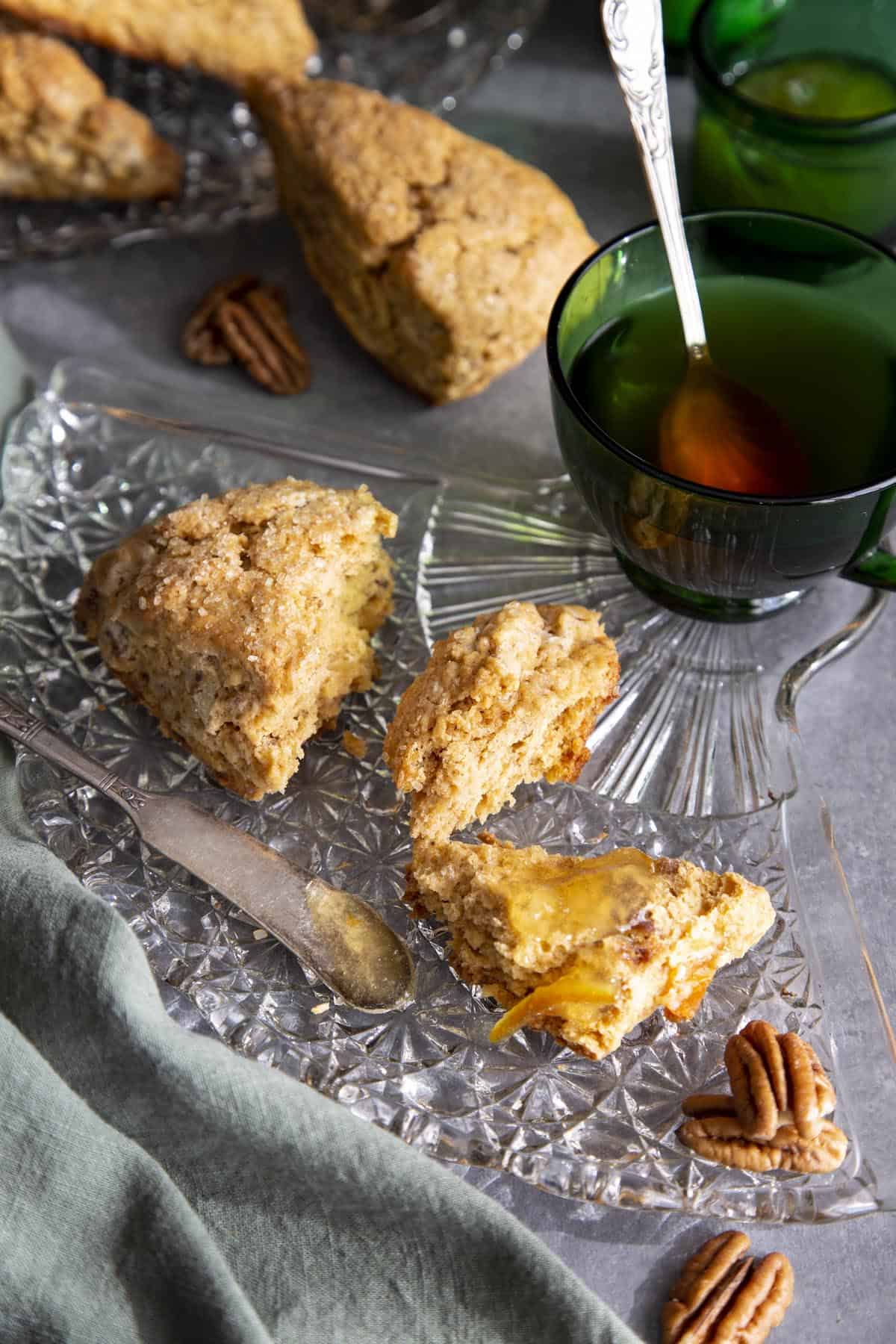 Cardamom Persimmon Pecan Scones Scone pieces with jam on a glass plate next to a green tea cup.