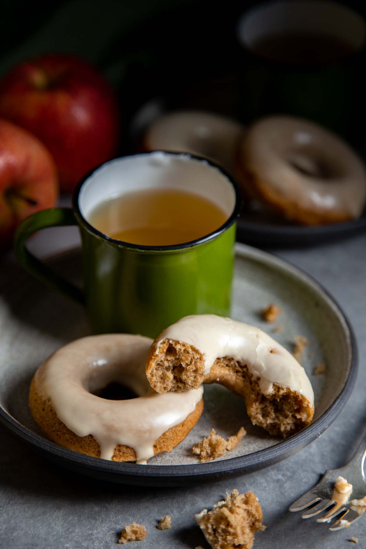 Half eaten apple donuts on a plate with a cup of tea