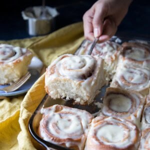 A hand picking up a cinnamon roll from the pan.