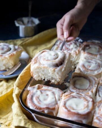 A hand picking up a cinnamon roll from the pan.