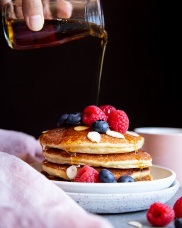 Pouring maple syrup on a stack of almond pancakes