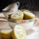 Green tea mochi in a tea cup being dusted with powdered sugar.