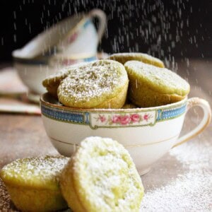 Green tea mochi in a tea cup being dusted with powdered sugar.