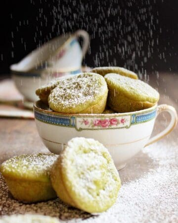 Green tea mochi in a tea cup being dusted with powdered sugar.