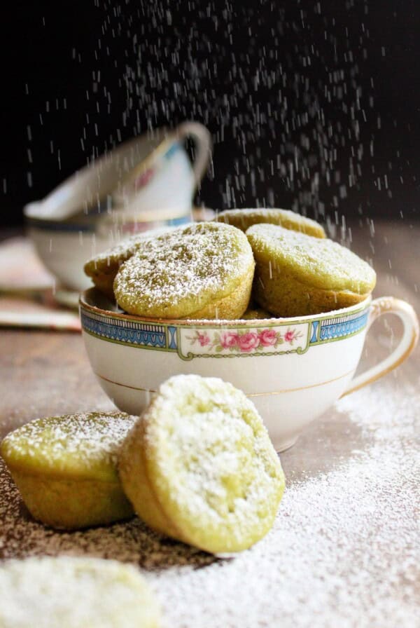 Green tea mochi in a tea cup being dusted with powdered sugar.