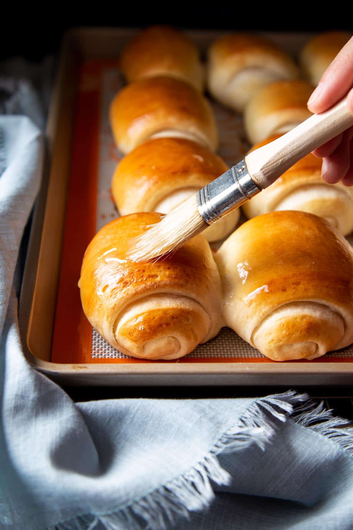 Brushing baked buttermilk rolls with melted butter.