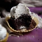 Half eaten cookies and cream cupcake on a purple surface.