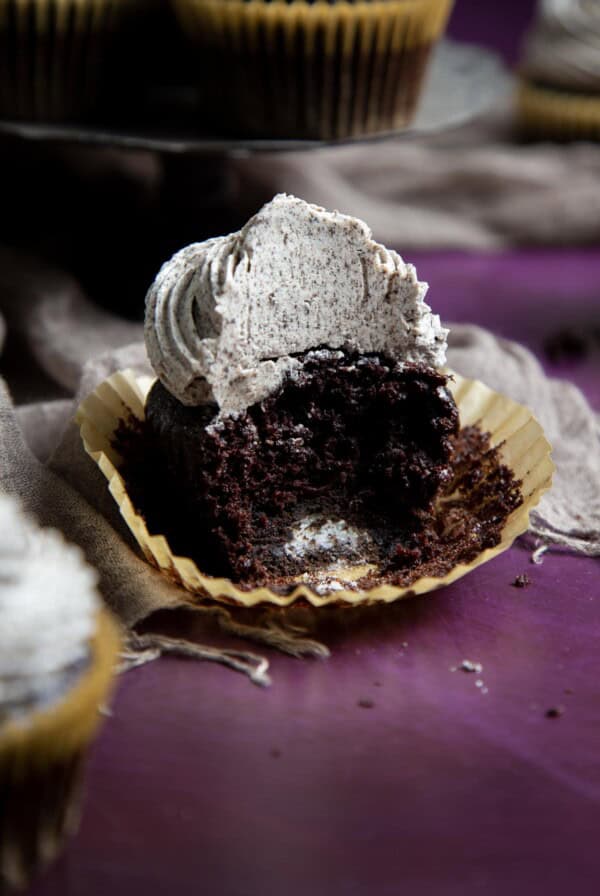Half eaten cookies and cream cupcake on a purple surface.
