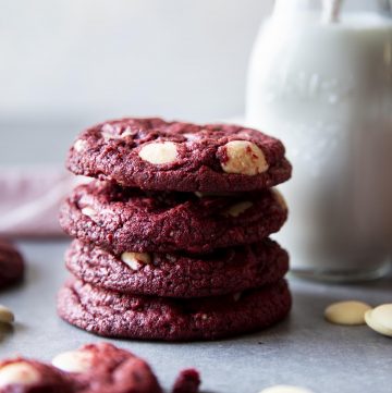 A stack of 4 red velvet cookies next to a bottle of milk