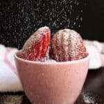Red velvet madeleines in a pink cup with powdered sugar falling down.