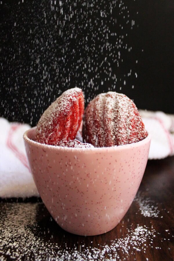 Red velvet madeleines in a pink cup with powdered sugar falling down.