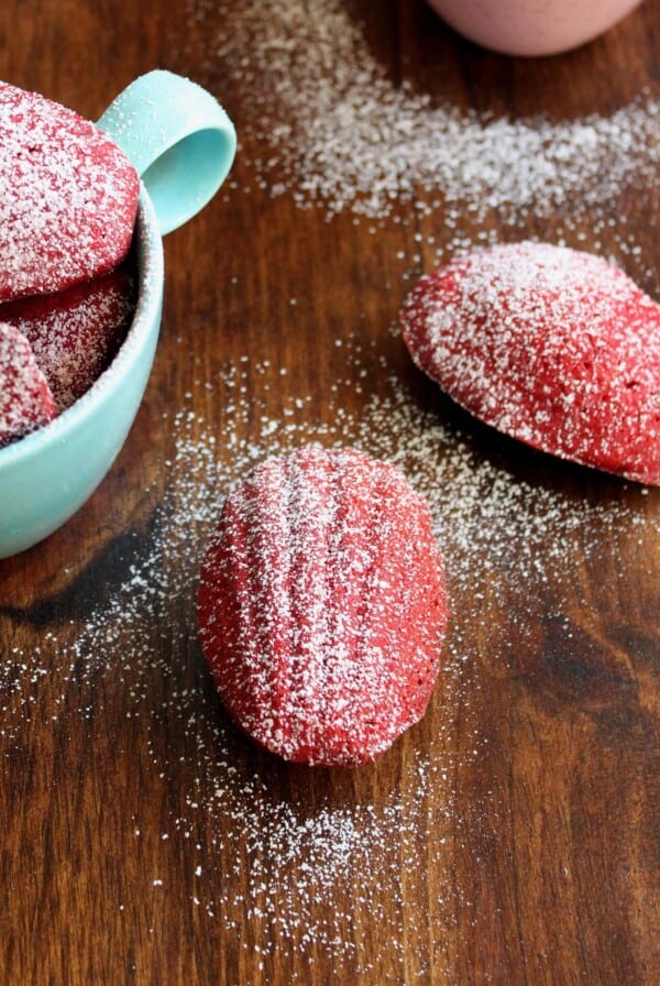 Red velvet madeleines in cups and on table top.