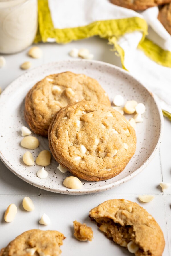 Three quarter view of a plate with two white chocolate and macadamia nut cookies.