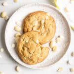 Two white chocolate macadamia cookies on a plate, one cookie has a bite taken out of it.