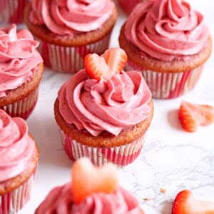 Strawberry champagne cupcakes garnished with strawberry heart cutouts on a white marble surface.