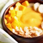 Close up image of a peach mango smoothie in a wooden bowl.