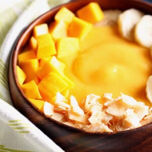Close up image of a peach mango smoothie in a wooden bowl.