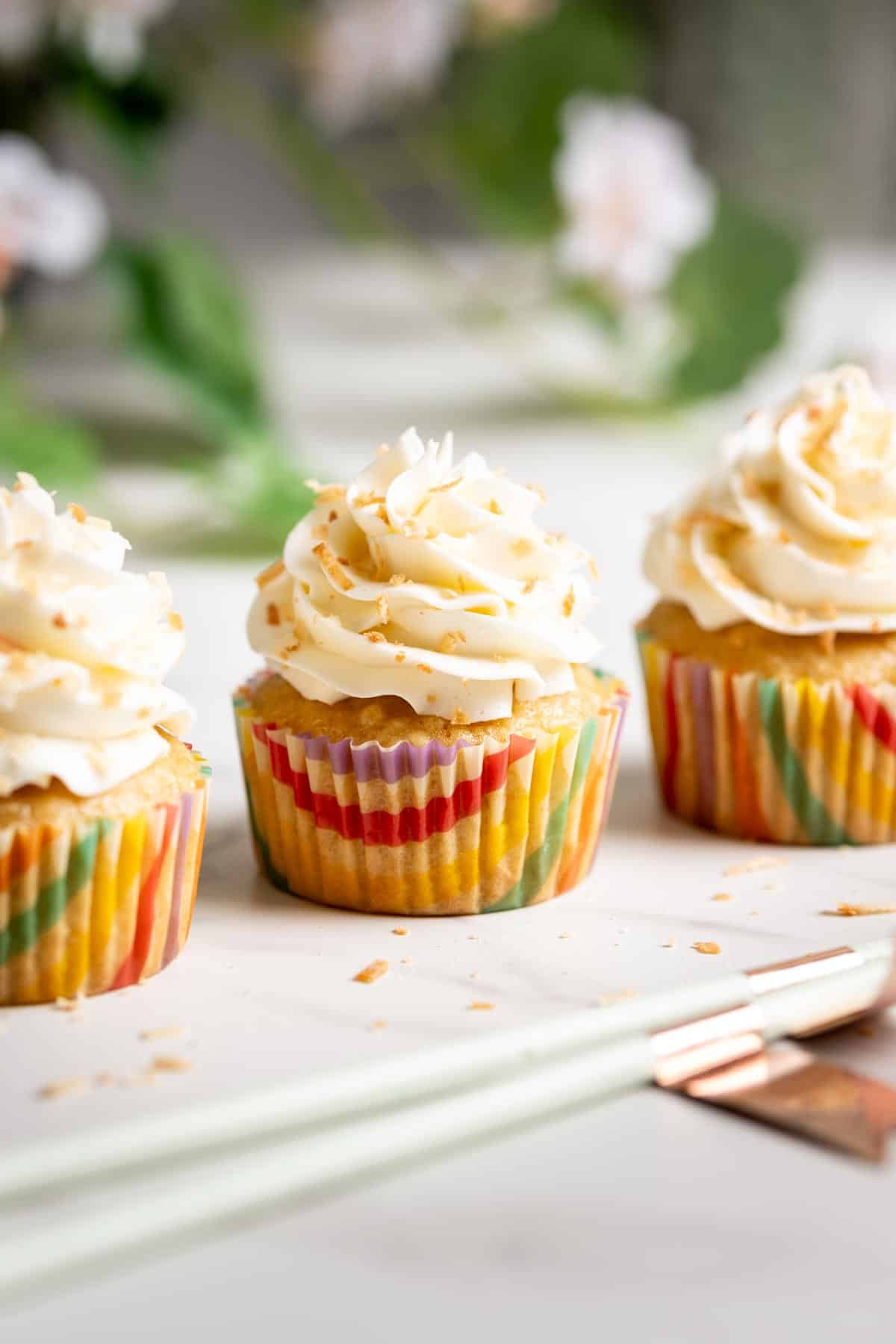 Three pina colada cupcakes lined up on a white marble surface.
