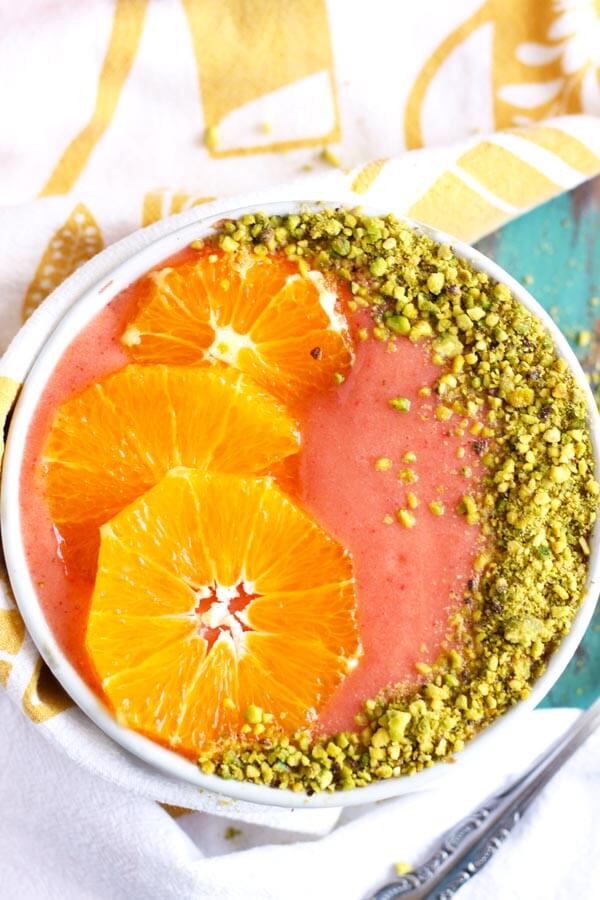 Strawberry orange smoothie in a bowl garnished with orange slices and pistachio