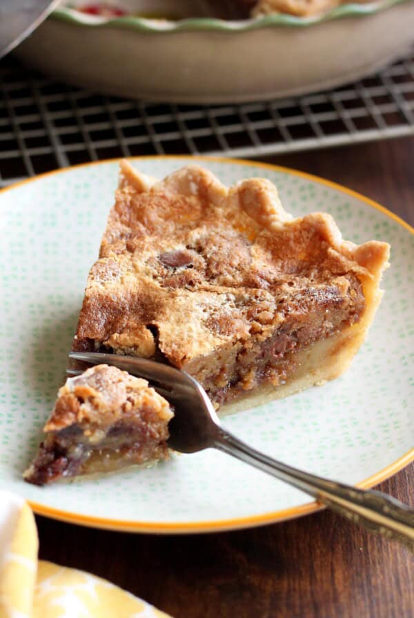 A slice of chocolate chip cookie pie on a plate with a fork cutting off a piece.