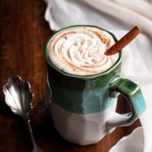 Pumpkin spice hot chocolate in a mug with whipped cream and a cinnamon stick.
