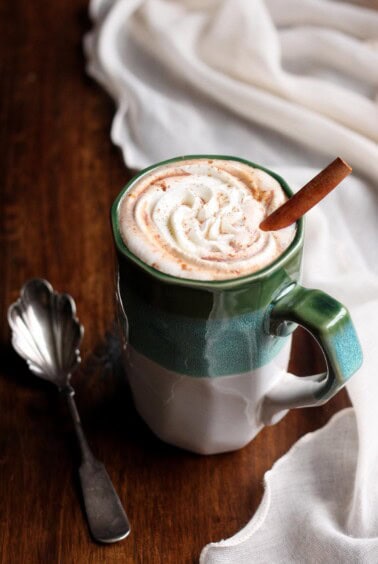 Pumpkin spice hot chocolate in a mug with whipped cream and a cinnamon stick.