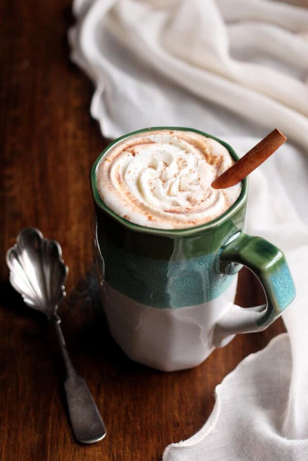 Pumpkin spice hot chocolate in a mug with whipped cream and a cinnamon stick.