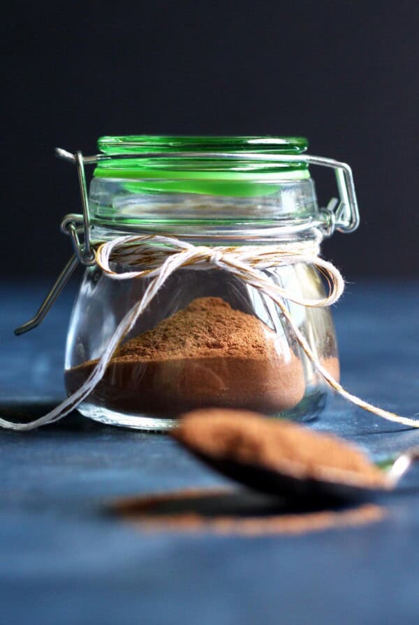 Pumpkin pie spice in a jar with a spoon of spice in front of it.