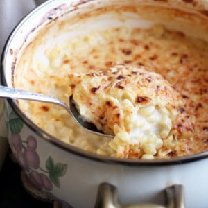 A serving spoon scooping some creamed corn au gratin from a pot.
