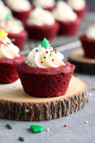 A red velvet cake cookie with cream cheese frosting is garnished with Christmas sprinkles.