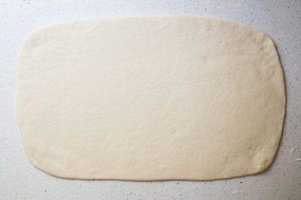 Mini Pigs in a Blanket (made with milk bread) A sheet of dough rolled out on a white countertop.