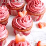 Pink strawberry champagne cupcakes sitting on a white marble surface with strawberry heart cutouts.