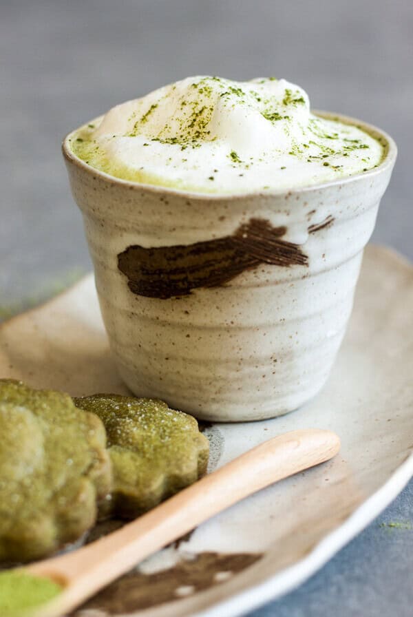 Matcha latte in a tea cup on a plate with a couple matcha cookies next to it.