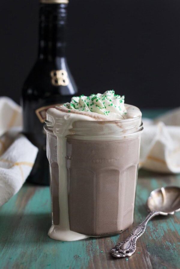 Irish cream hot chocolate with whipped cream in a glass jar, spilling over the side.