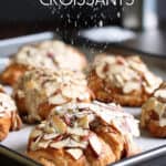A tray of almond croissants with powdered sugar falling over them.