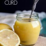 Lemon curd in a jar with a spoon in it next to some lemons
