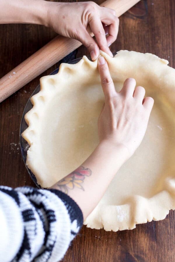 Fluting the edge of pie crust in a pie pan.
