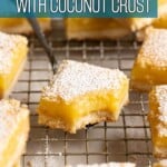 A half eaten square of lemon bar on small serving utensil sitting among powdered sugar dusted lemon squares.