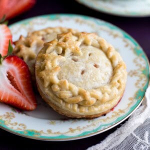 Two decorated Strawberry Hand Pies on a plate with fresh strawberries.