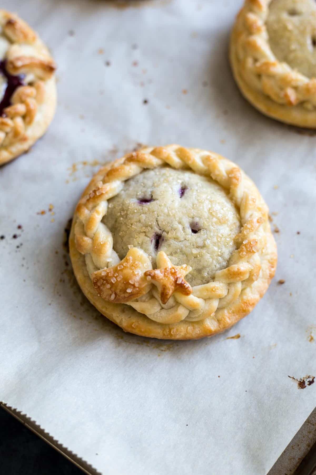 Blueberry and lemon make a perfect pair like peanut butter and jelly. They come together in this recipe to bring you these pretty Mini Blueberry Pies! #wildwildwhisk #miniblueberrypies Baked mini blueberry pies on a baking sheet.